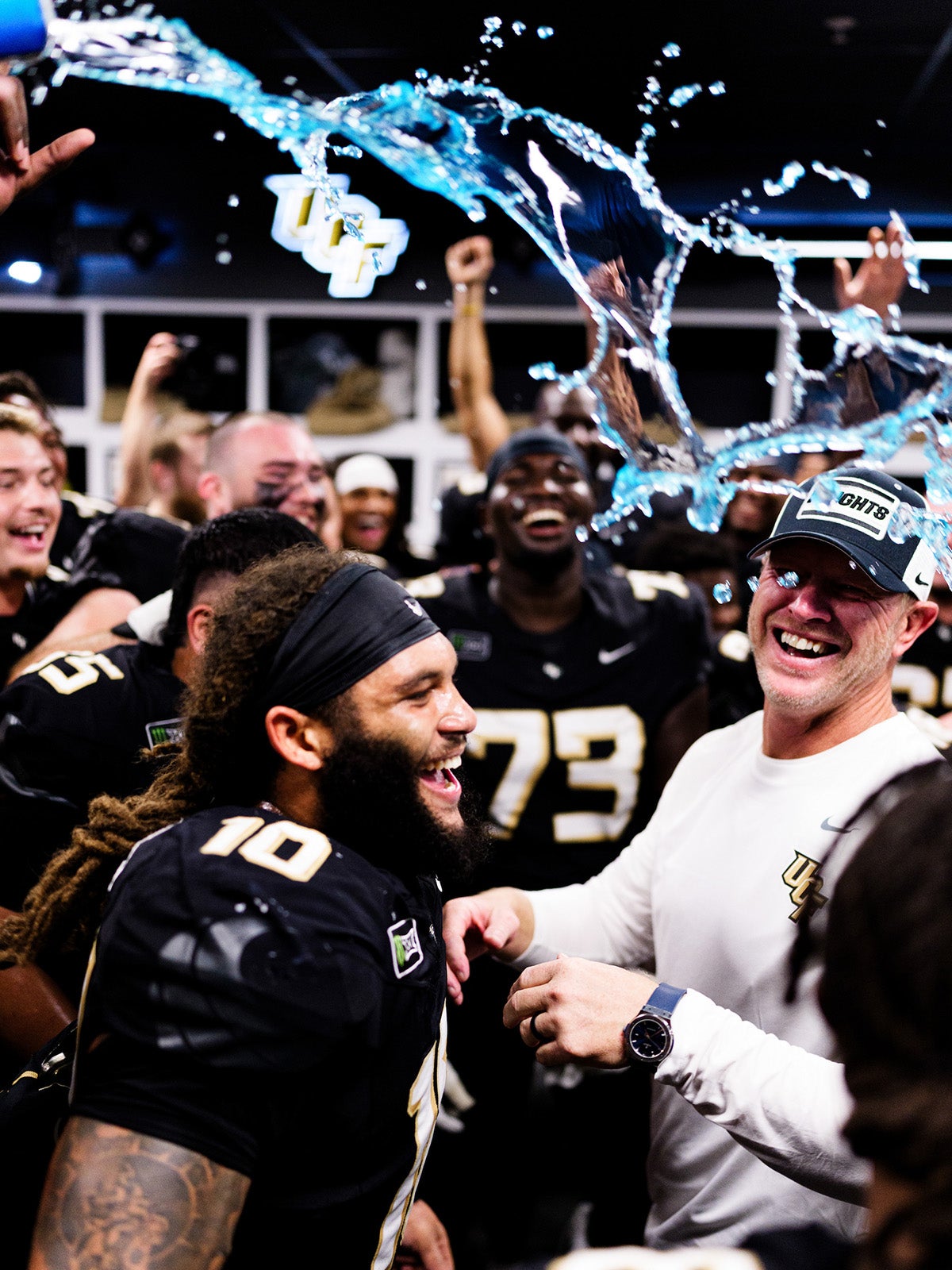 UCF head coach Scott Frost celebrates with players in locker room as blue liquid flies overhead 