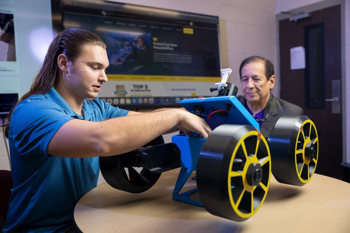 UCF aerospace engineering graduate student Carson Gray works on a rover prototype as industrial engineering Professor Luis Carlos Rabelo looks on.