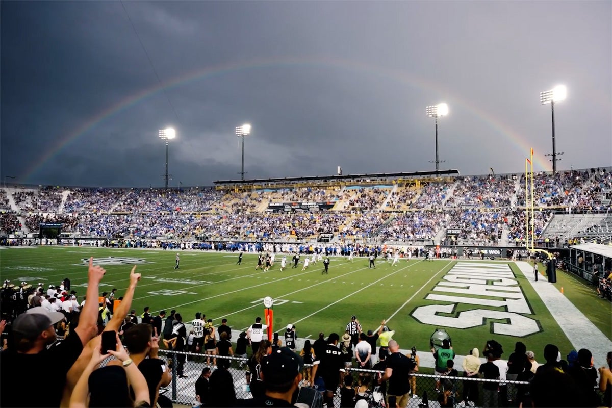 A rainbow arch against a gray sky above wide angle of UCF football stadium