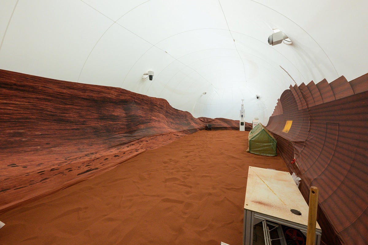 A simulated Mars environment with red dirt, fake Mars landscape as wallpaper and white dome ceiling