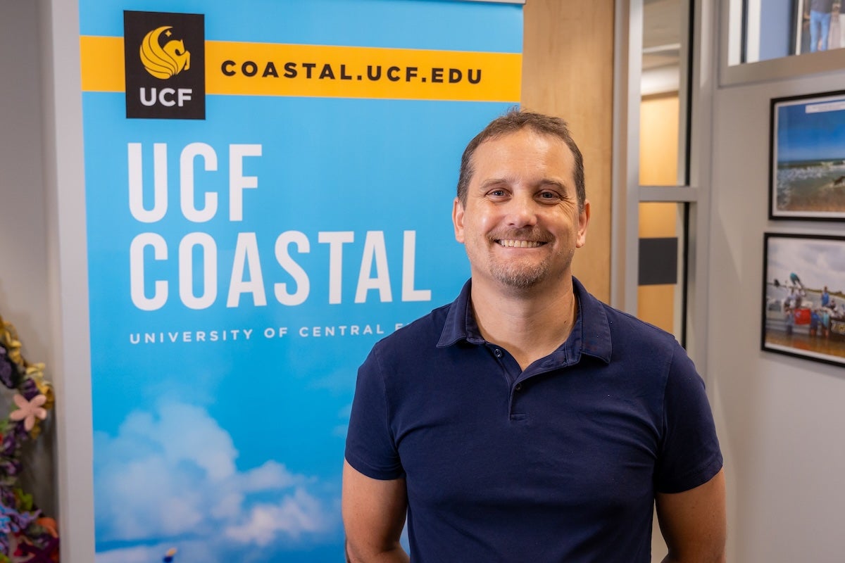 Professor Ivan Haigh stands in front of a sky blue poster for the UCF Coastal faculty research cluster.