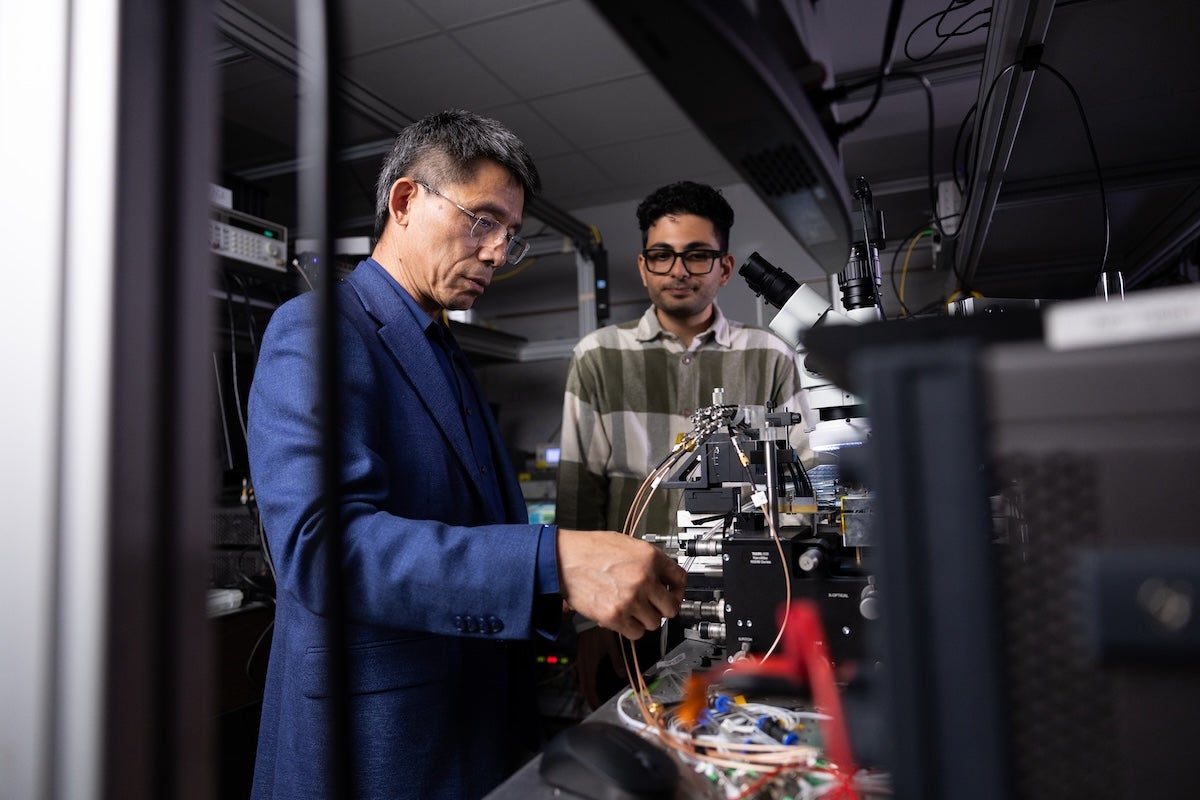 UCF optics and photonics professor Guifang Li and researcher Matin Dehghani stand beside optical research equipment in a CREOL laboratory.