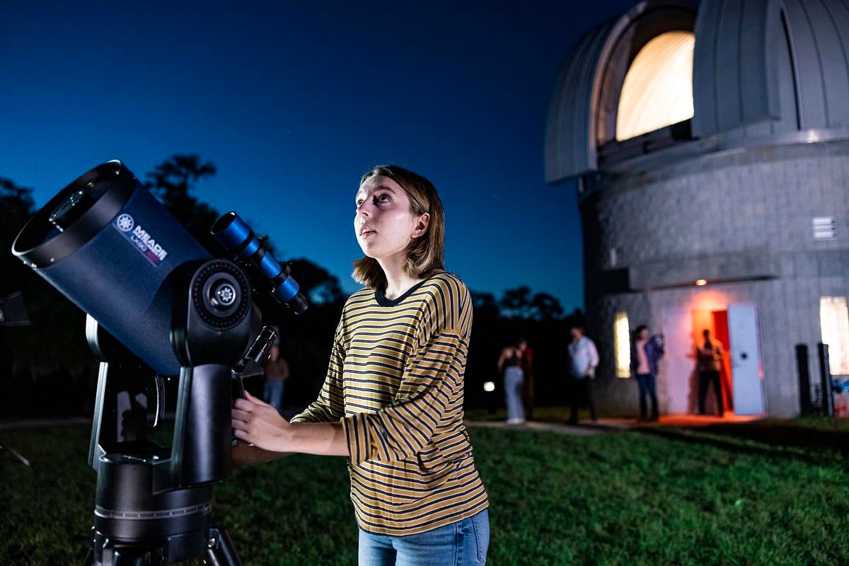 A person looking up while touching a telescope as UCF's Robinson Observatory is behind them
