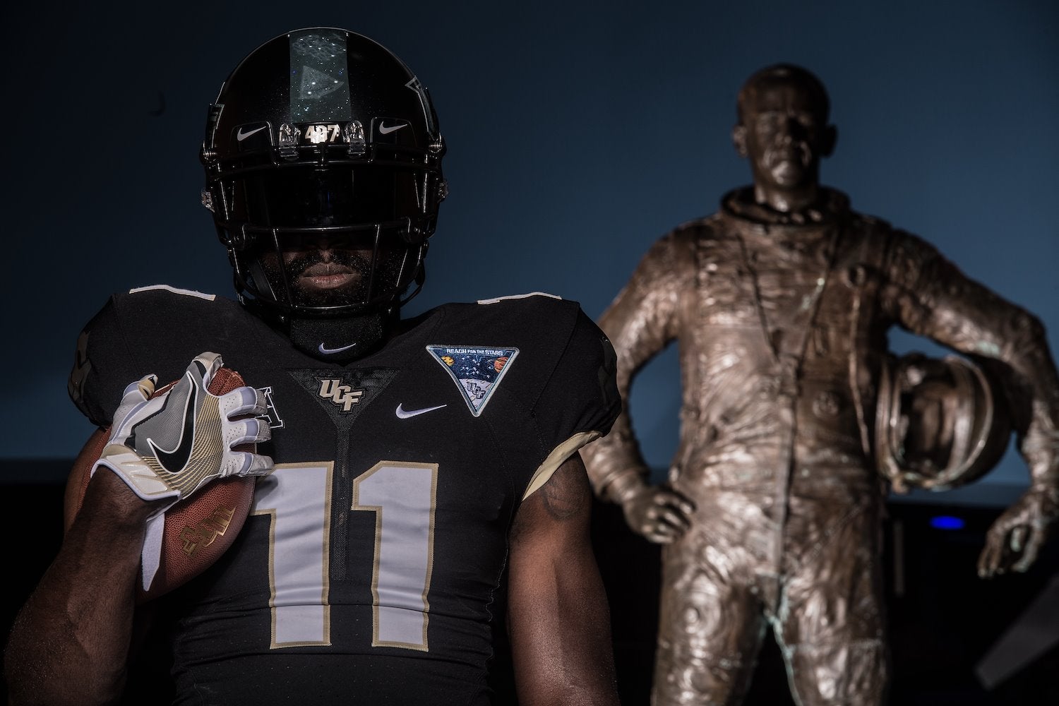A football player in uniform posing next to a statue of an astronaut