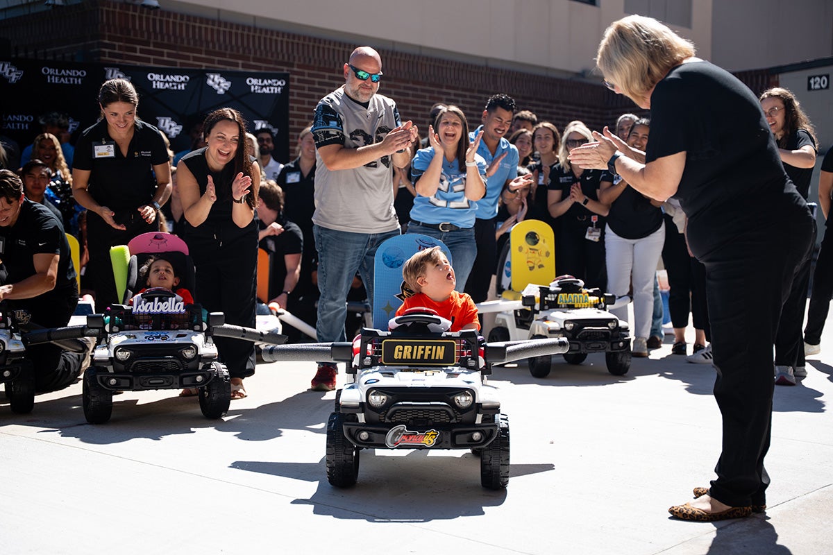 UCF physical therapy faculty member Jennifer Tucker leads cheers of parents and students as young children drive modified toy cars on pavement