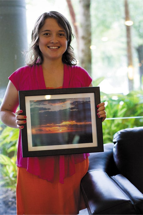 Young woman holding up a painting donated by a client to the Aphasia House