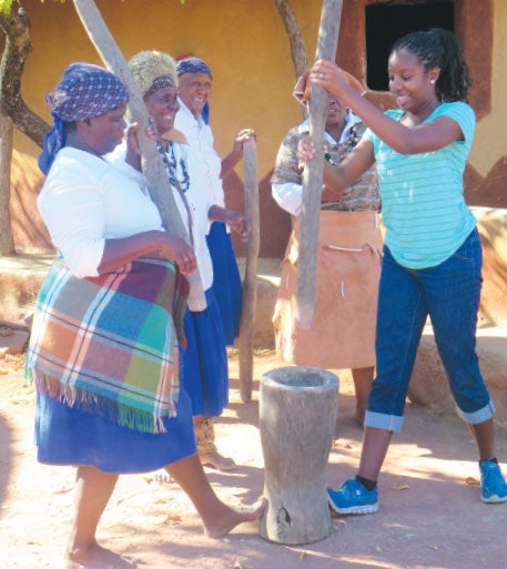 A UCF student helps women pound grain during an exchange program in Botswana.