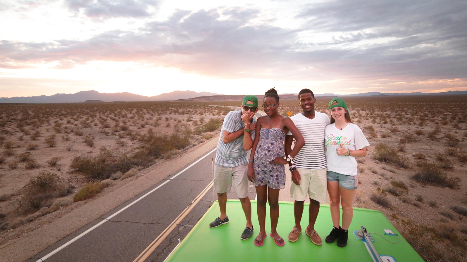 The cast of Roadtrip Nation posing on top of their travel bus