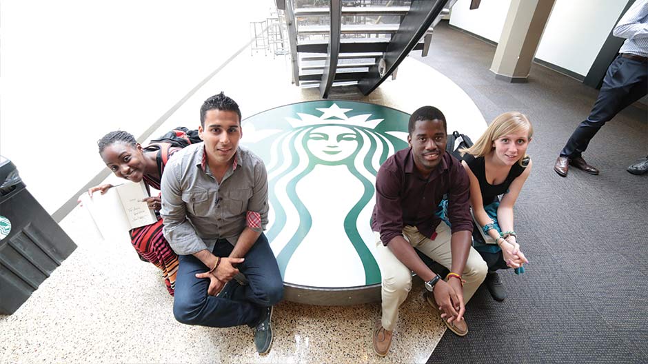 Four people sitting on a bench that has the Starbucks logo on it
