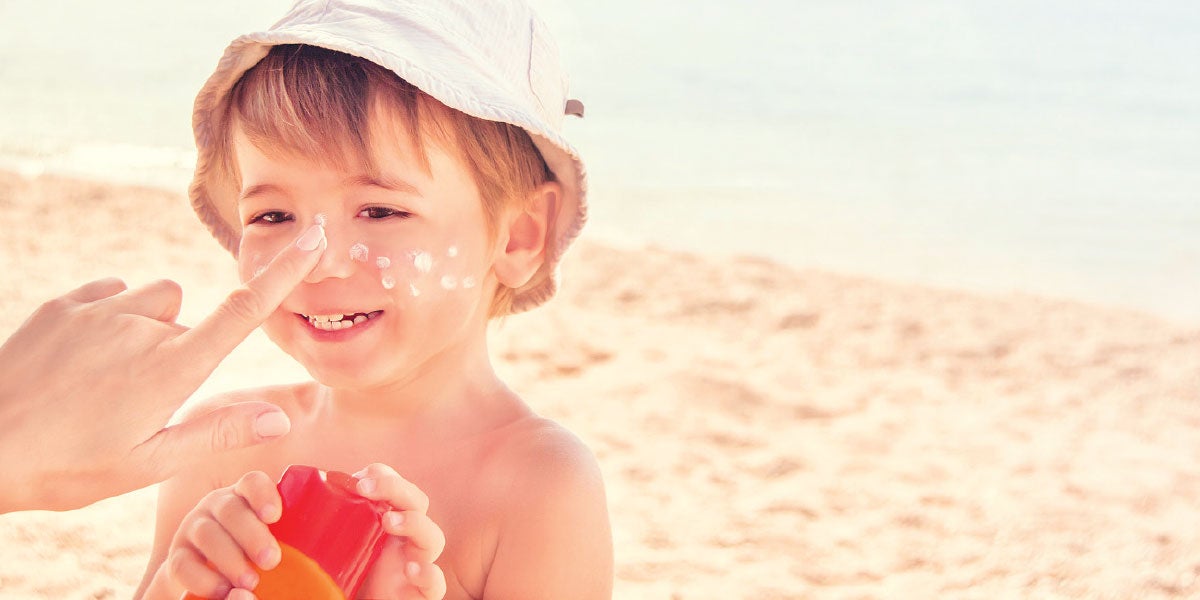 Hand placing sunscreen on a small boy at the beach