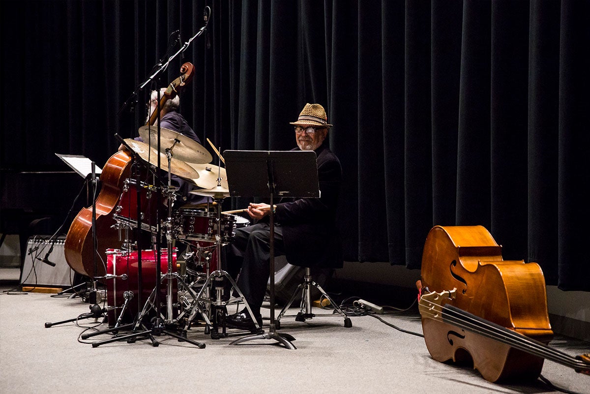 UCF Instructor Marty Morell plays the drums. He is looking a music stand. An upright base lies on its side to the right of him.