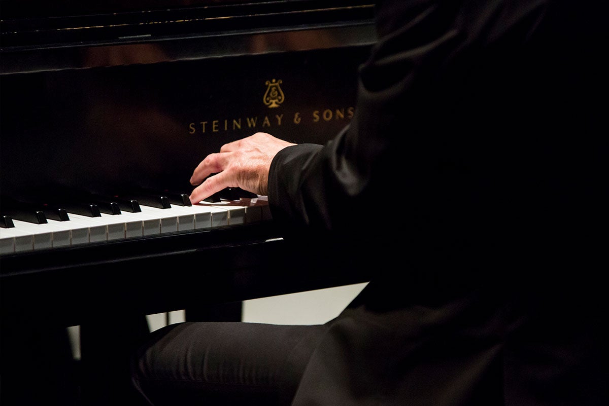 Hands are seen playing the keys of a Steinway piano.