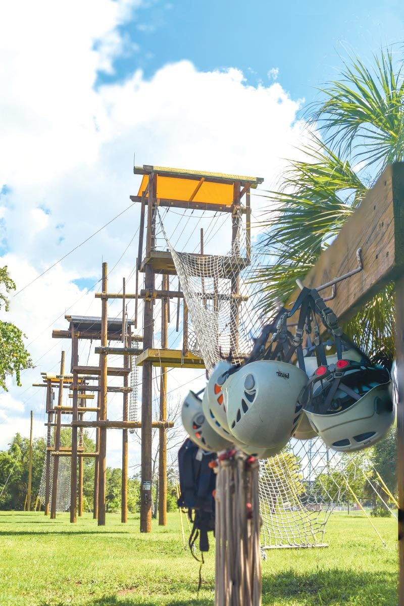 Helmets hang on the side of an empty high-elements climbing course made of ropes, wires, and wooden platforms and support beams.