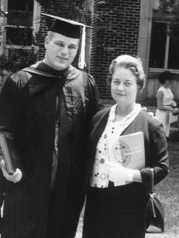 A black and white photo of man in academic regalia, including cap, gown and hood, standing next to an older woman.