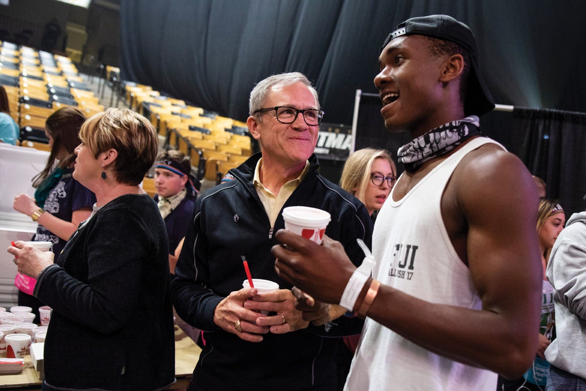 Dale Whittaker smiles and holds a smoothie as he listens to a male student speak.