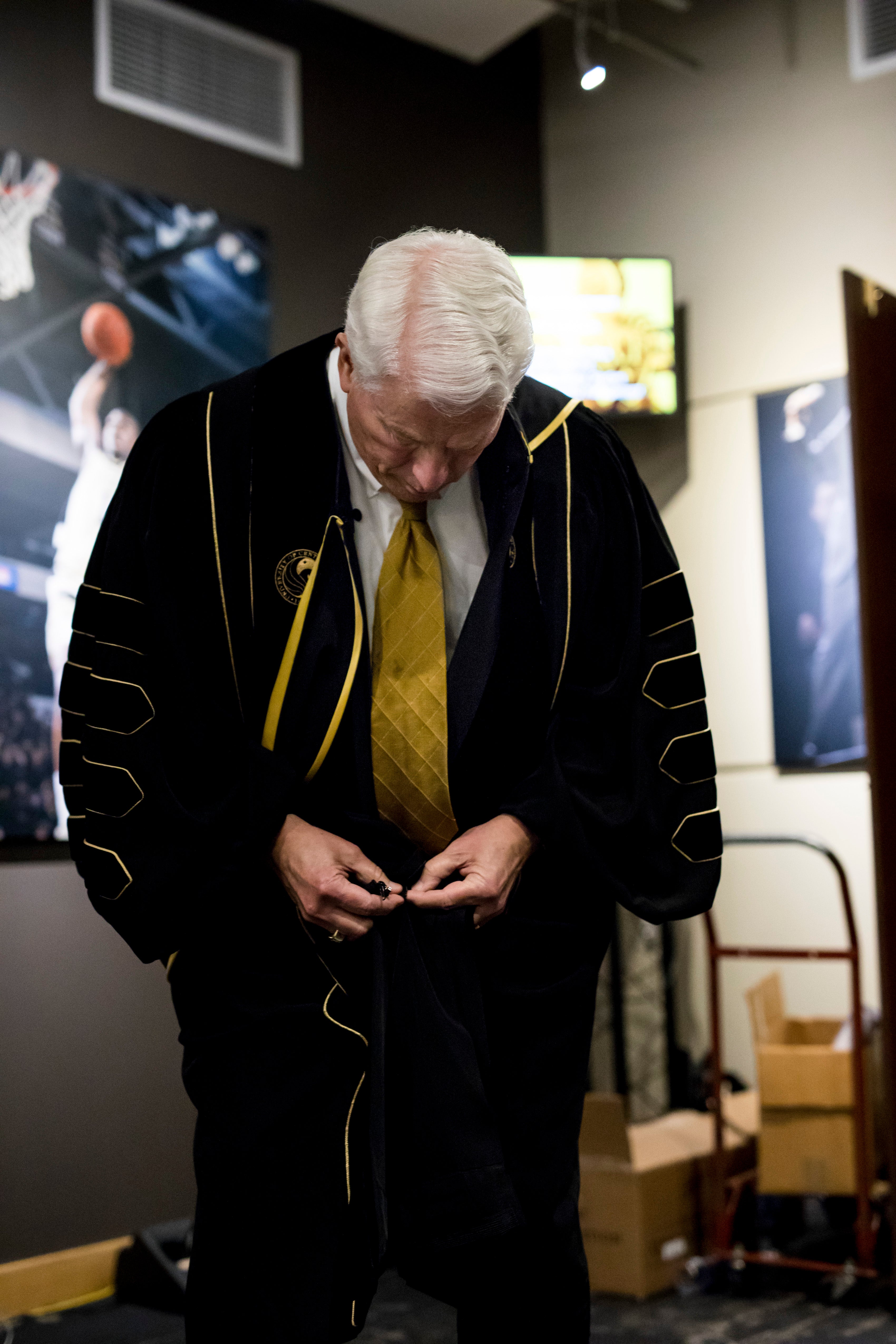 John C. Hitt looks down as he begins zipping his graduation gown up.