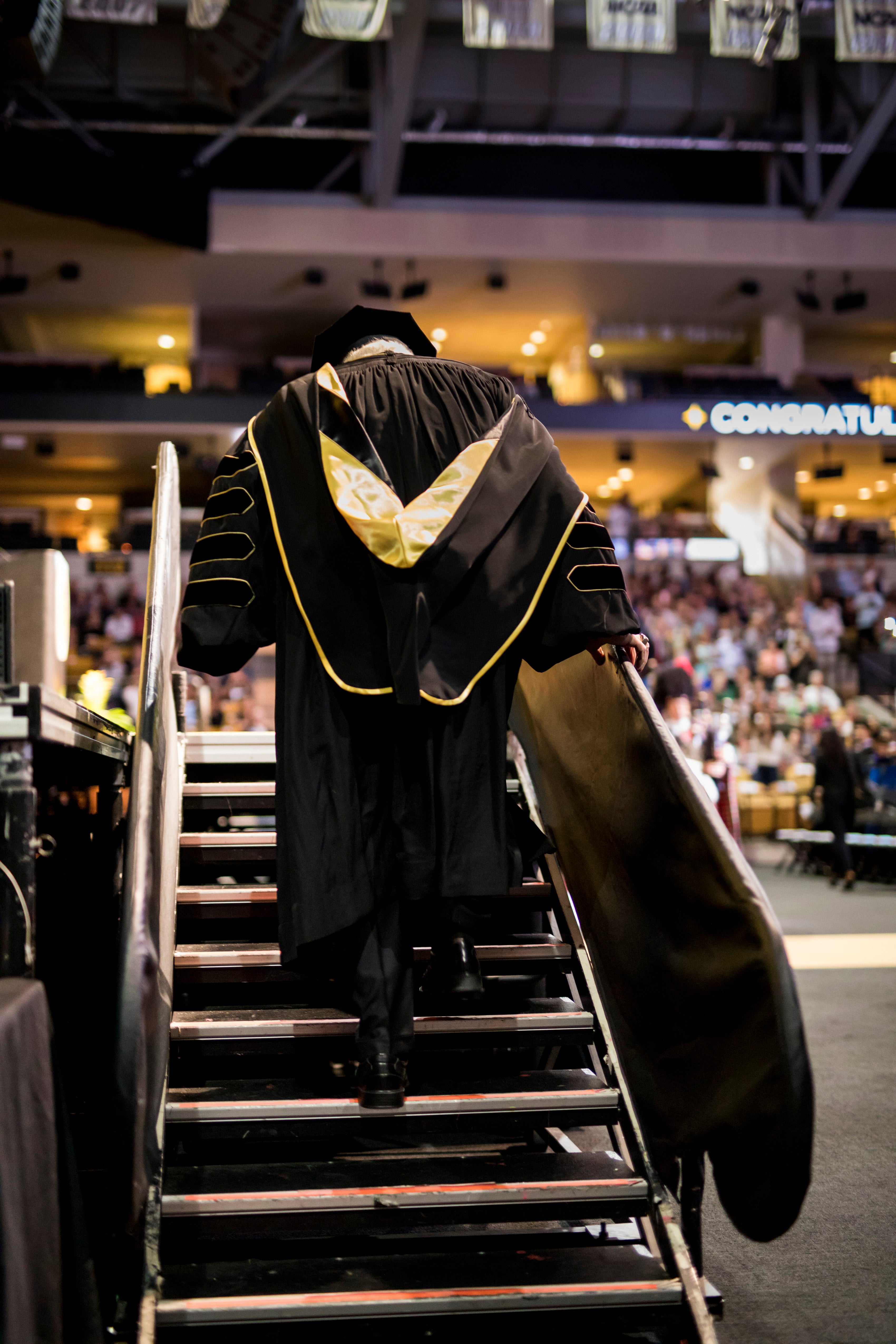 The back of John C. Hitt’s gown displays black and gold as he walks up the steps to the CFE Arena stage.