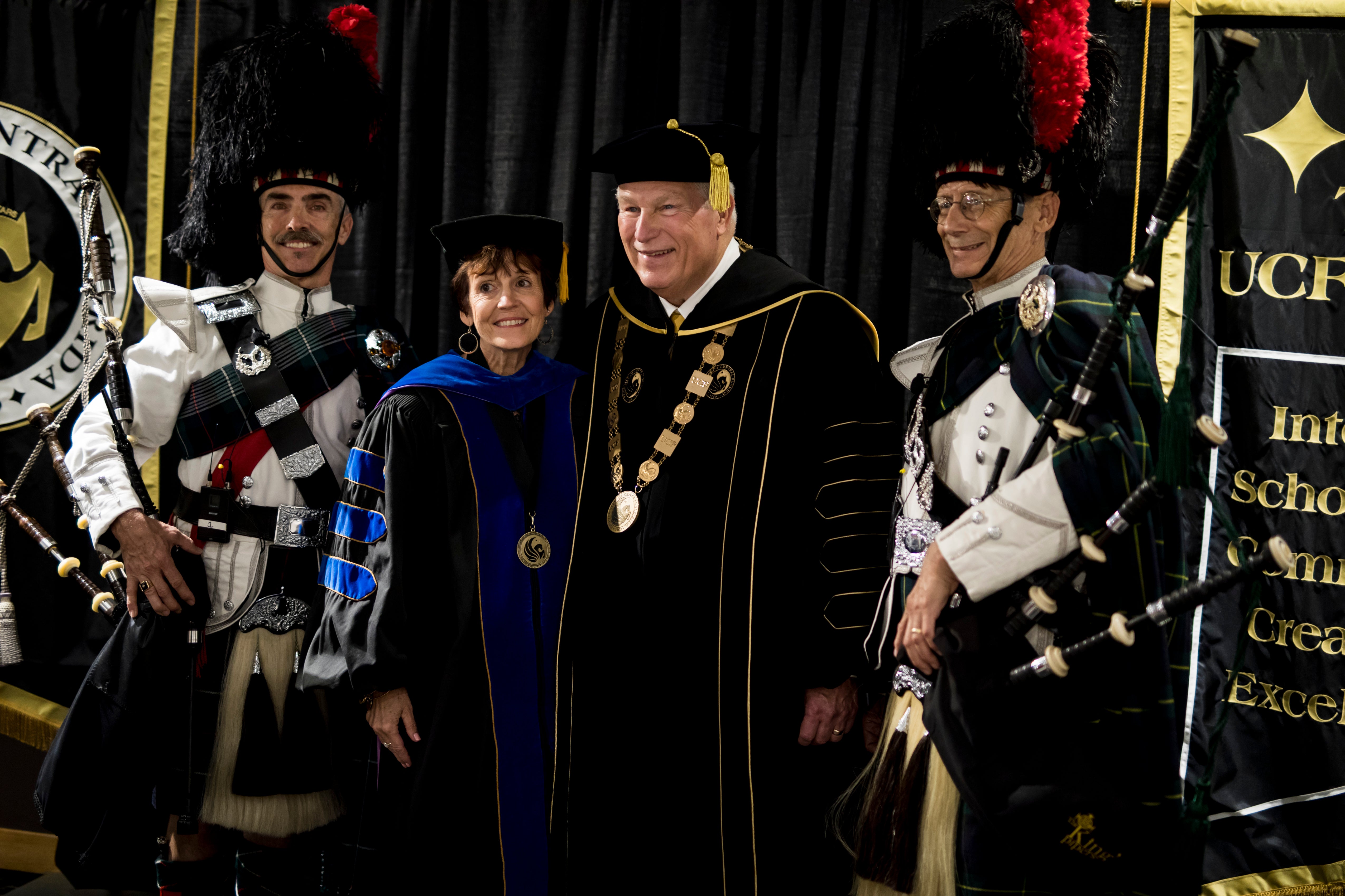 John C. Hitt poses beside a woman as two bagpipe players stand on either side of them for a photo.
