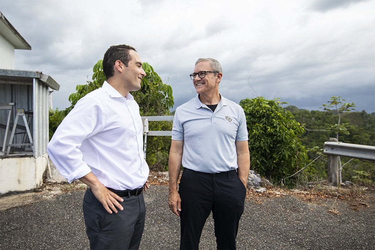 President Dale Whittaker wearing grey UCF polo, black pants and glasses, smiling at man with white shirt, grey pants, and his hands on his hips at Arecibo.