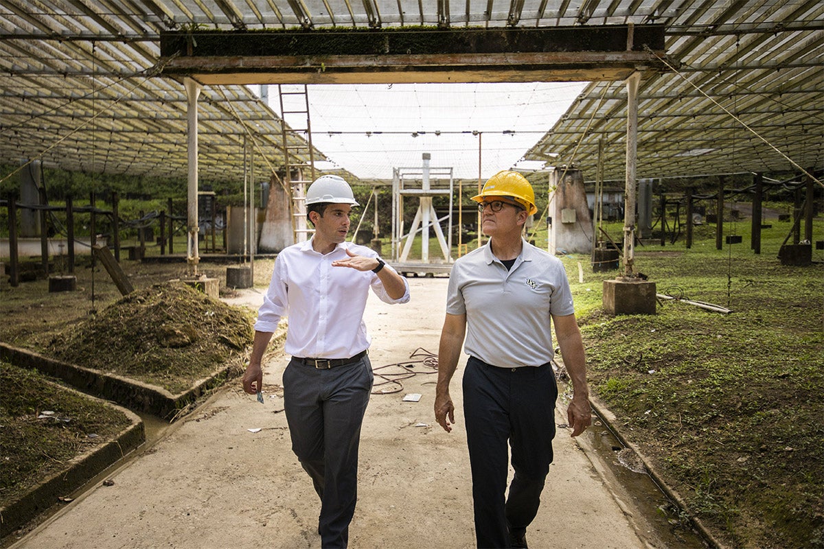 Concerned President Dale Whittaker walking with man talking about Arecibo and using hand gestures, both wearing hard hats.