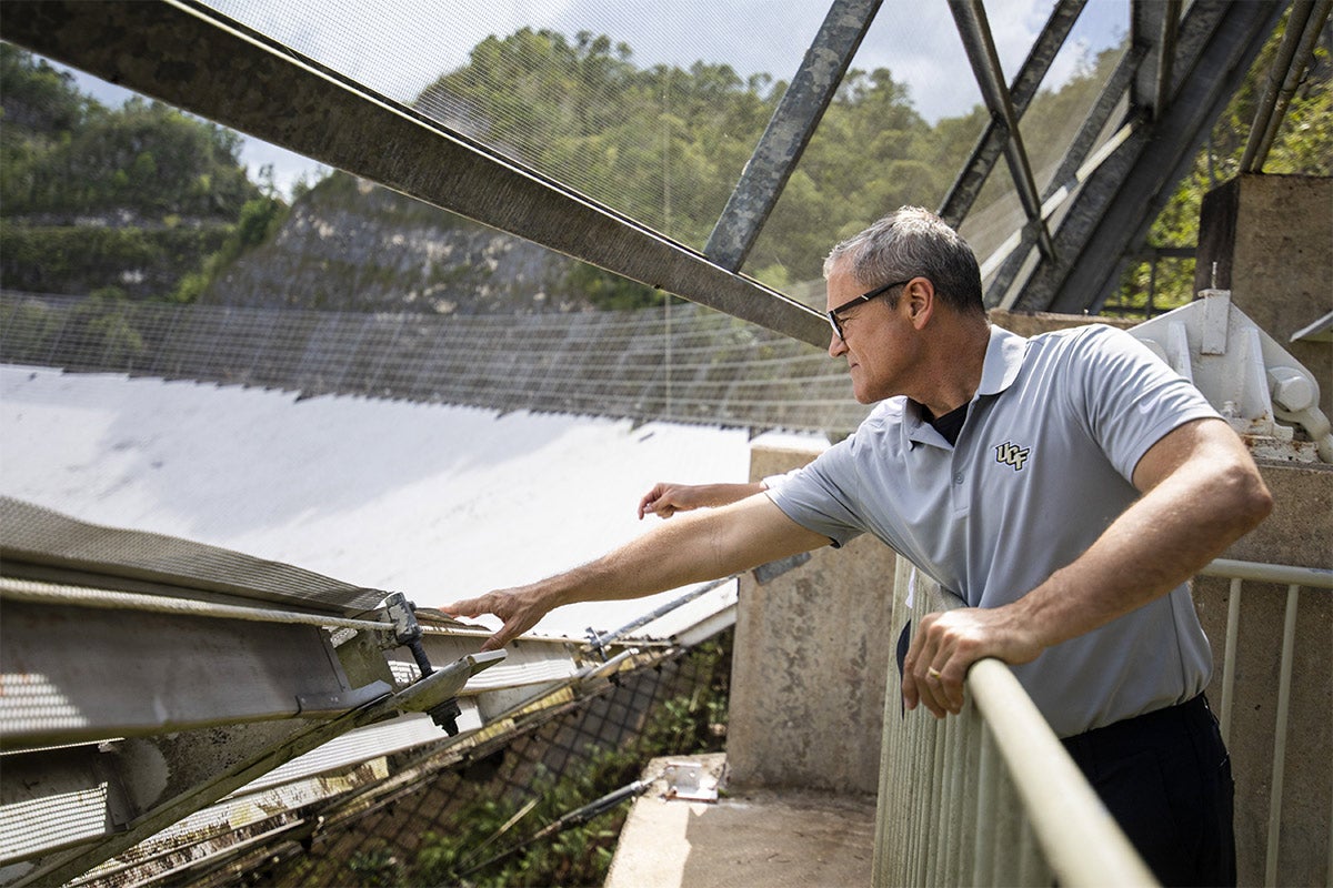 President Dale Whittaker reaches over guard rail to touch materials near Arecibo.