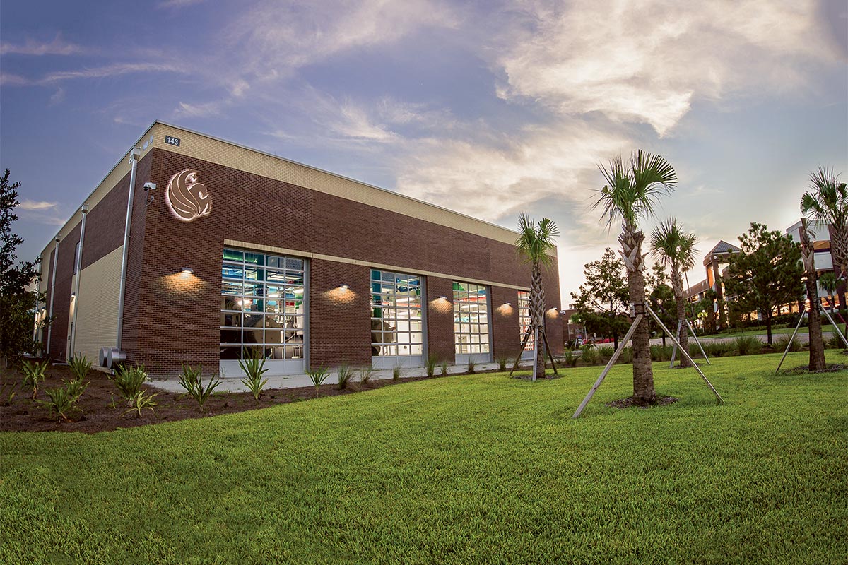 A large brick building with large windows and a pegasus symbol is lit up from the outside.