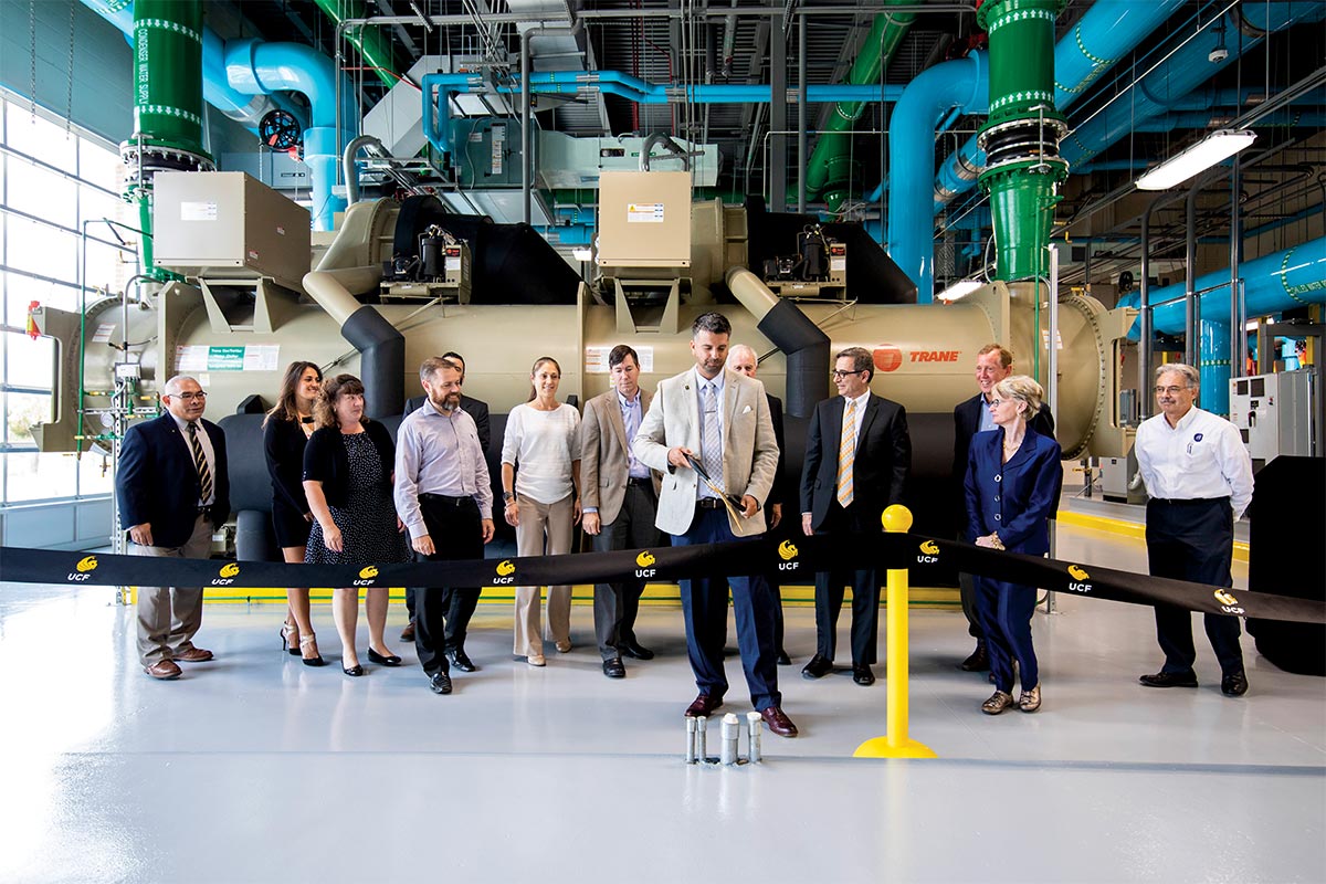 A man gets ready to cut a ribbon with a crowd of people, centrifugal chiller and colored pipes stand behind him.