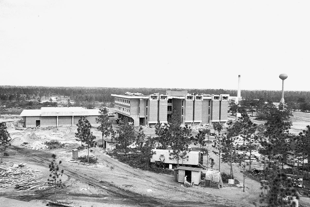 A black and white image shows a construction site with a finished building and trees.
