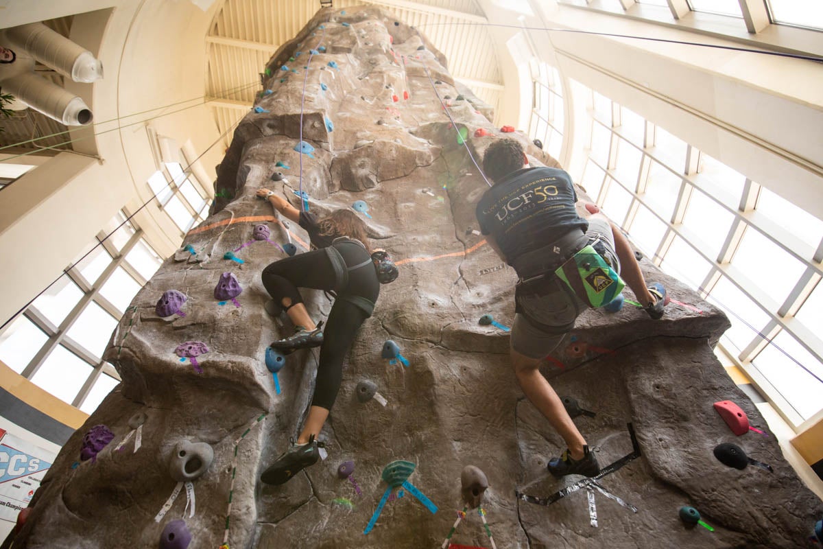 Two students climb a rock climbing wall.
