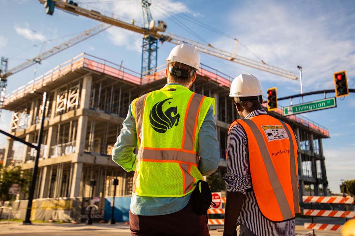 Two construction workers face an unfinished building.