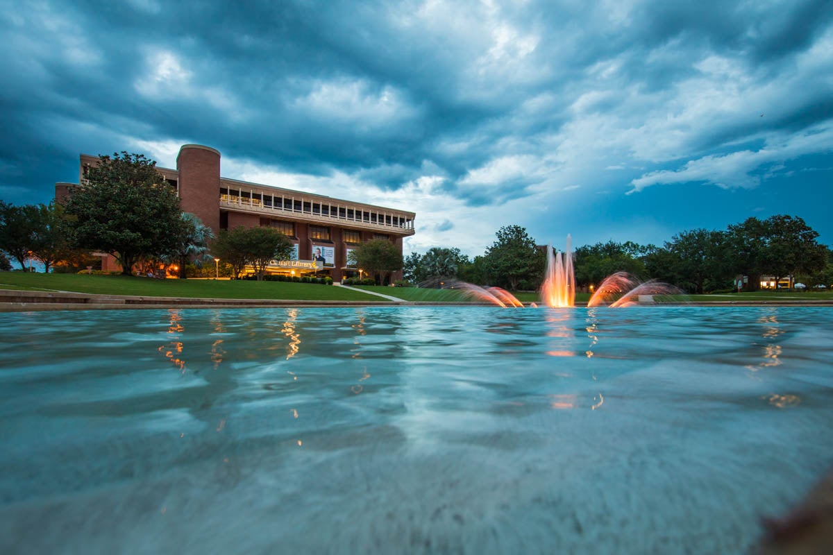 Lights brighten up the fountain of a pond in front of a library.
