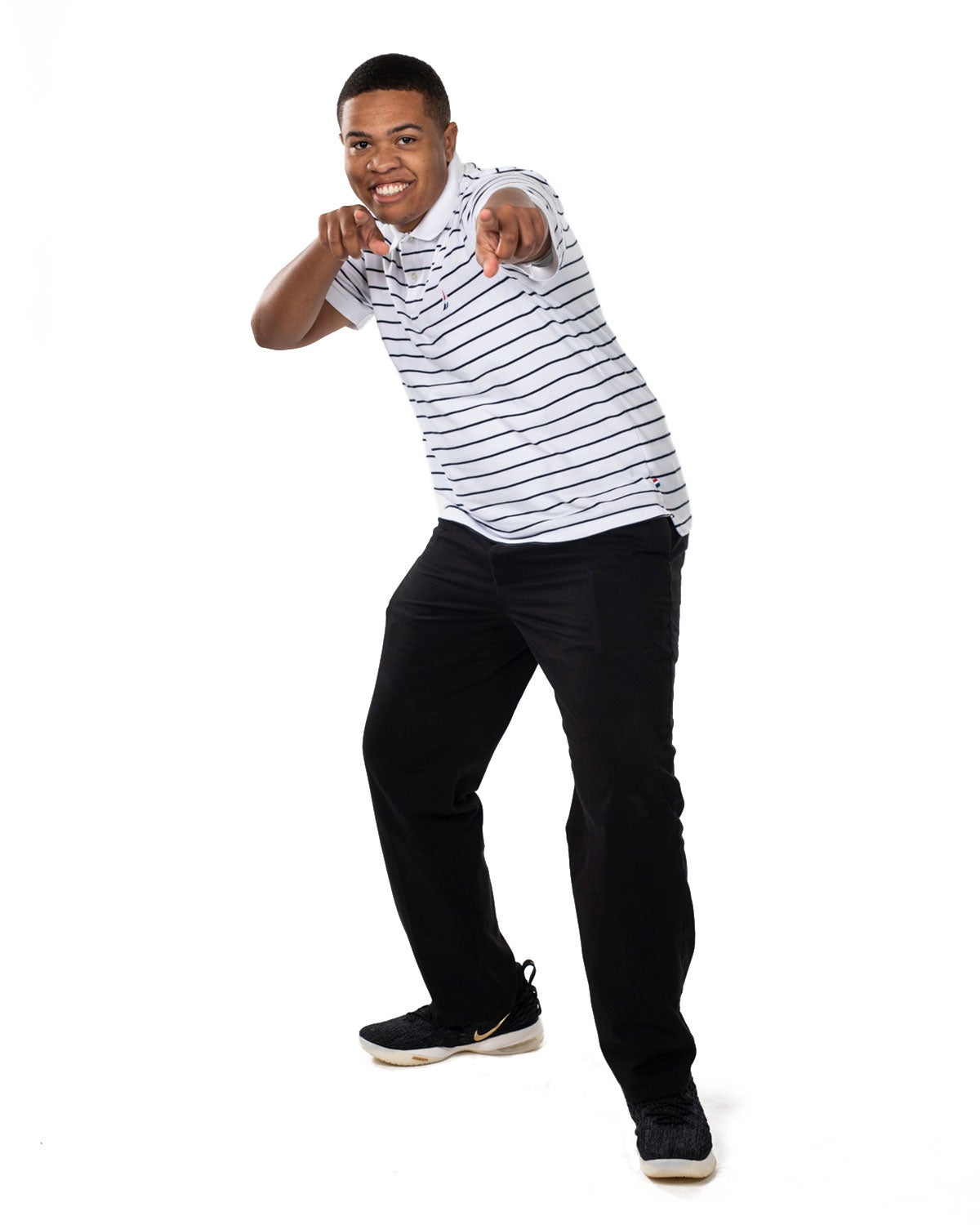 A man in a white and black striped shirt points to the camera and smiles.