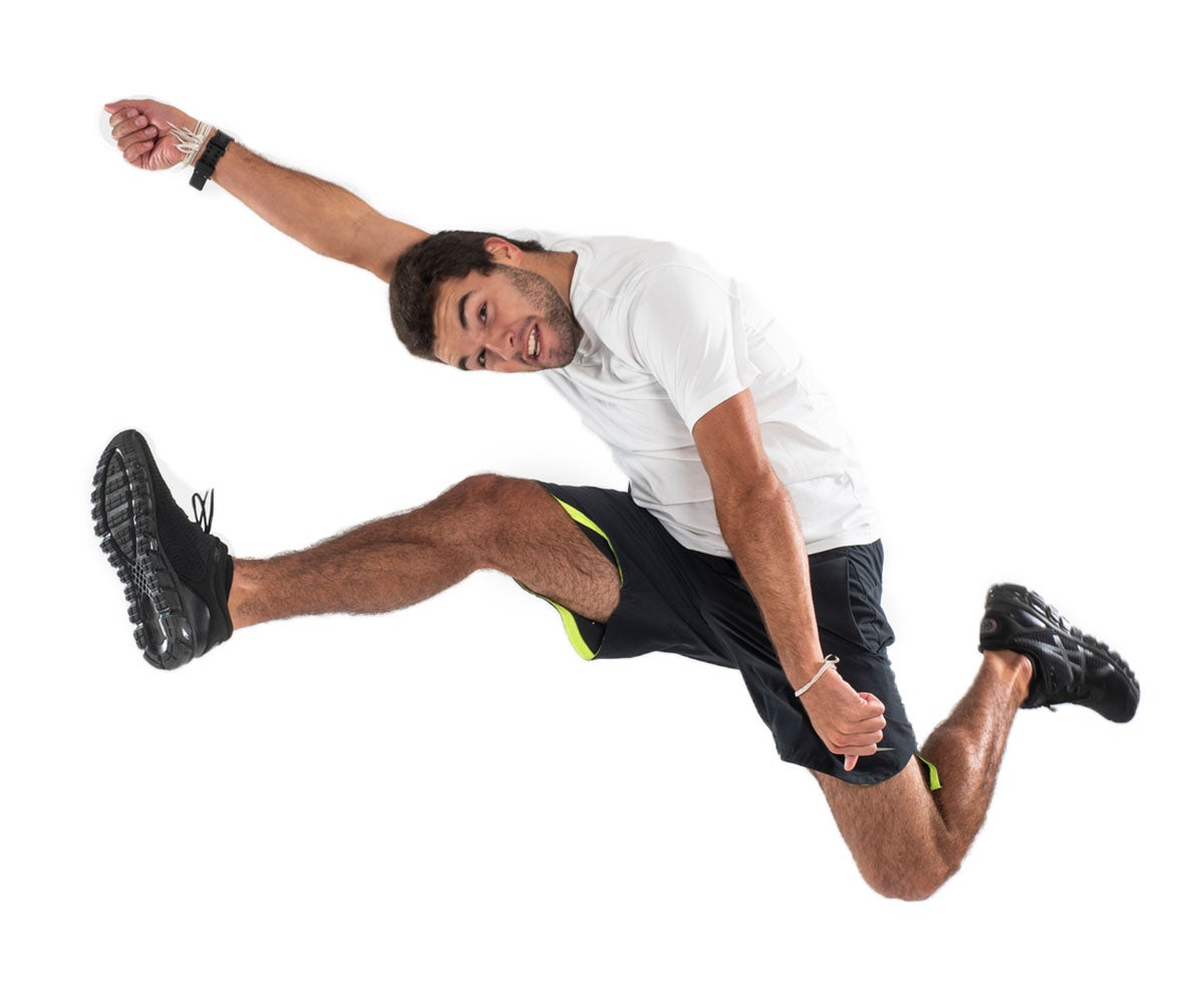 A man in a white shirt and black shorts jumps into the air as he stretches his arms.