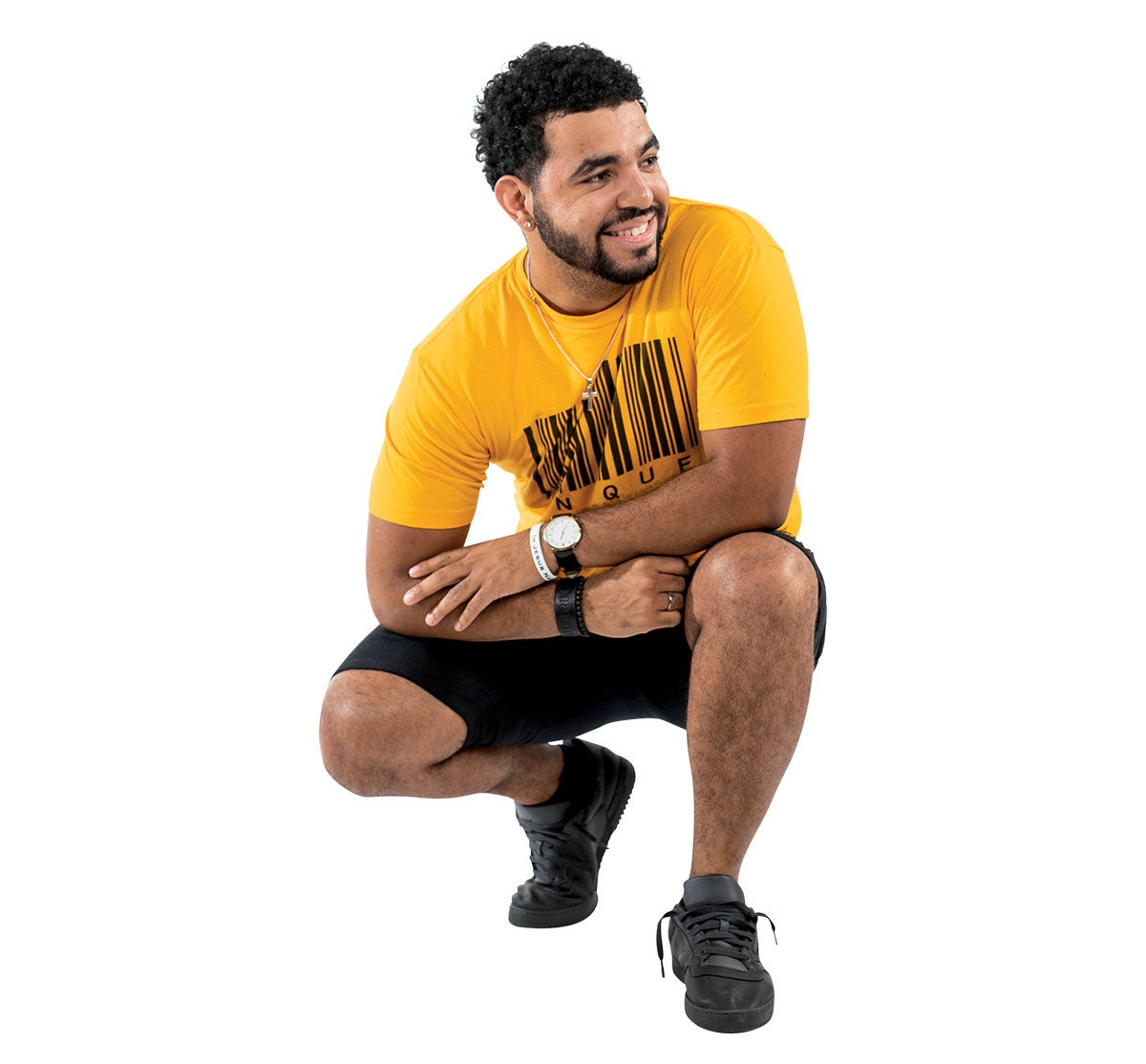 A man in a yellow shirt and black shorts crouches down while he looks to the side and smiles.