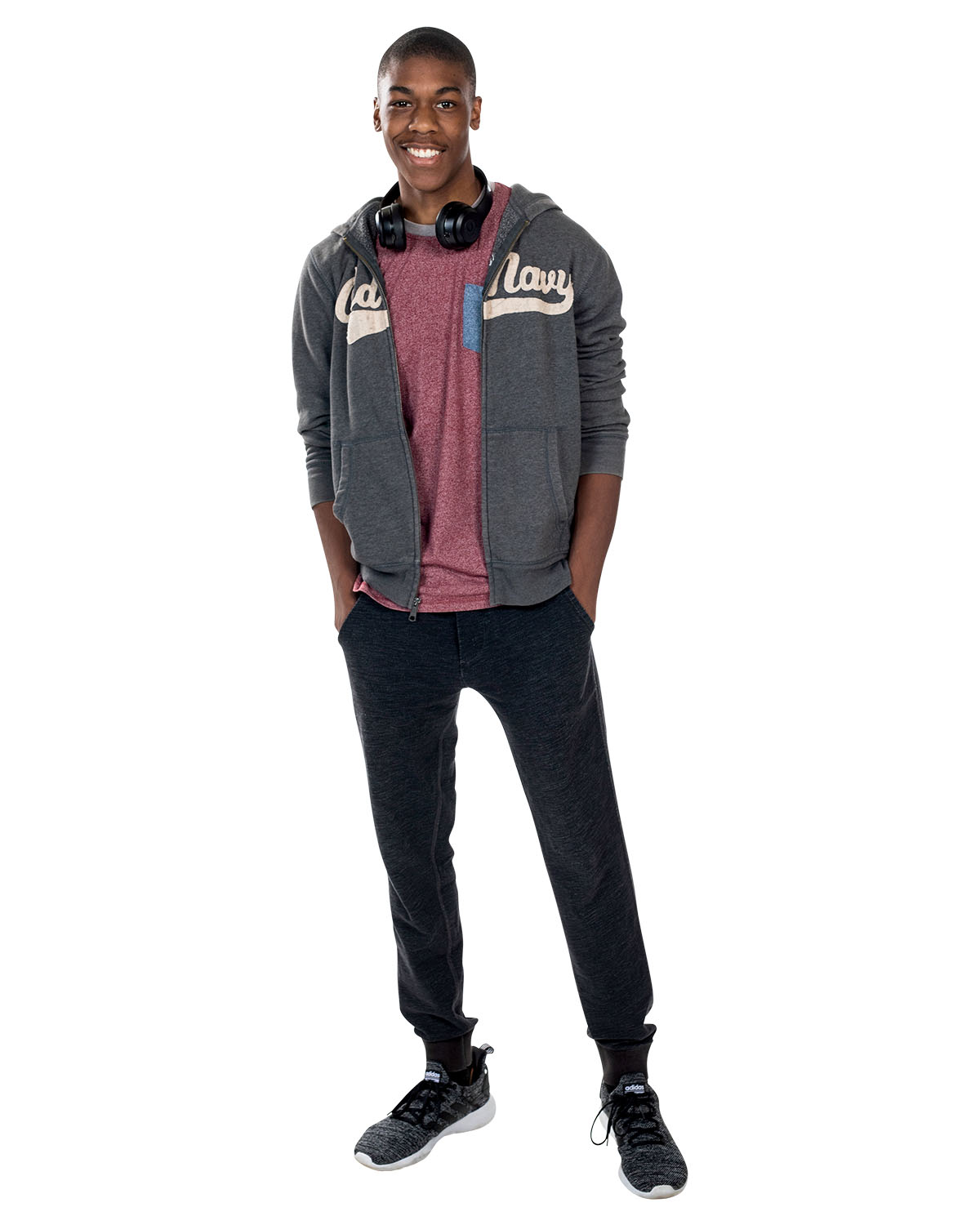 A man in black pants, red shirt and grey hoodie poses with headphones around his neck and his hands in his pockets. A man in black pants, red shirt and grey hoodie poses with headphones around his neck and his hands in his pockets.