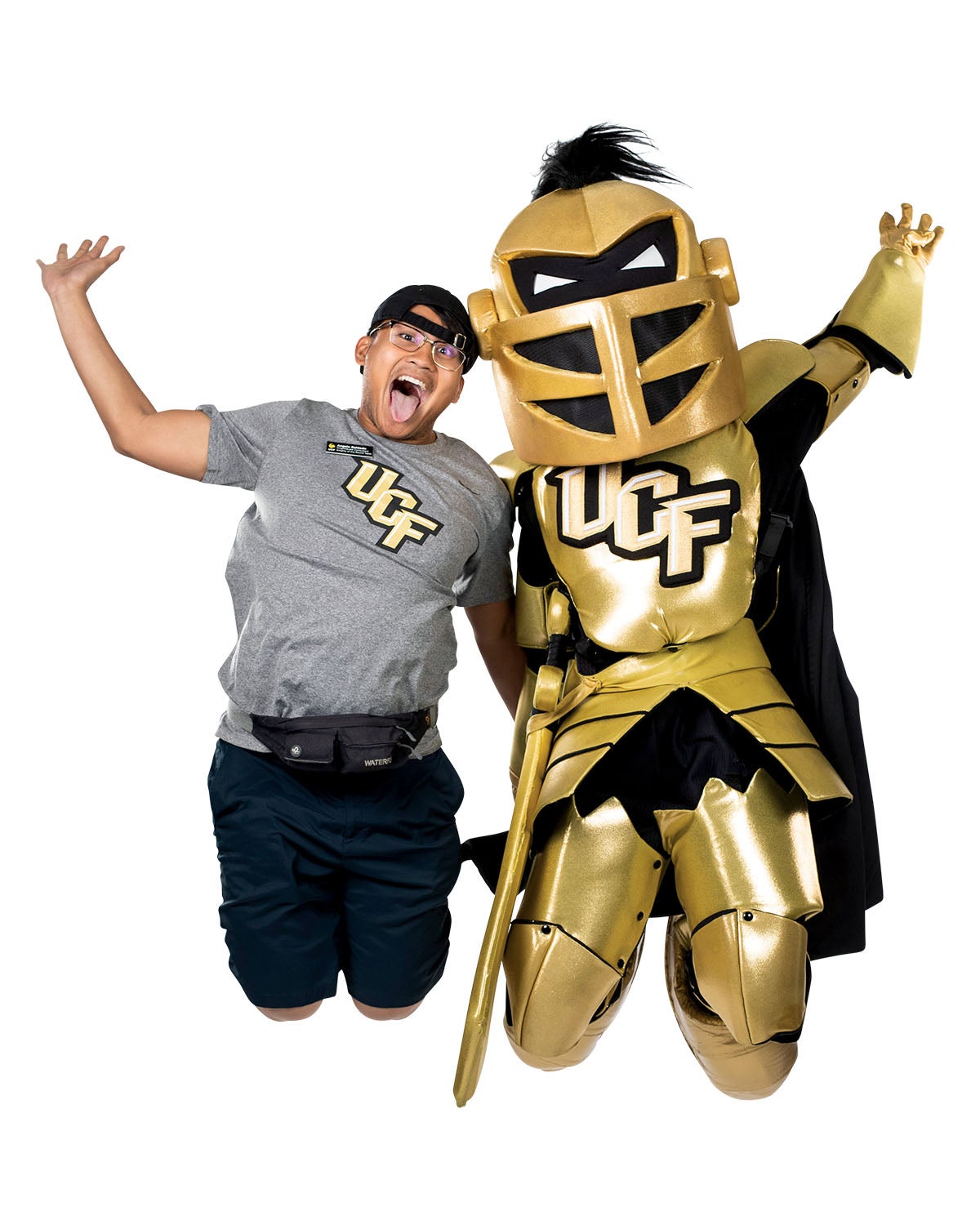 A man wearing a grey UCF shirt jumps in the air along someone in a knight costume.