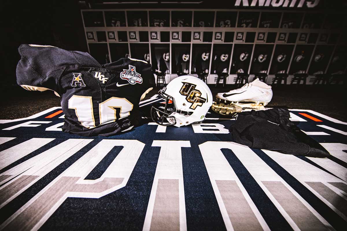 white helmet with gold UCF letters and a black jersey with cleats on a black carpet