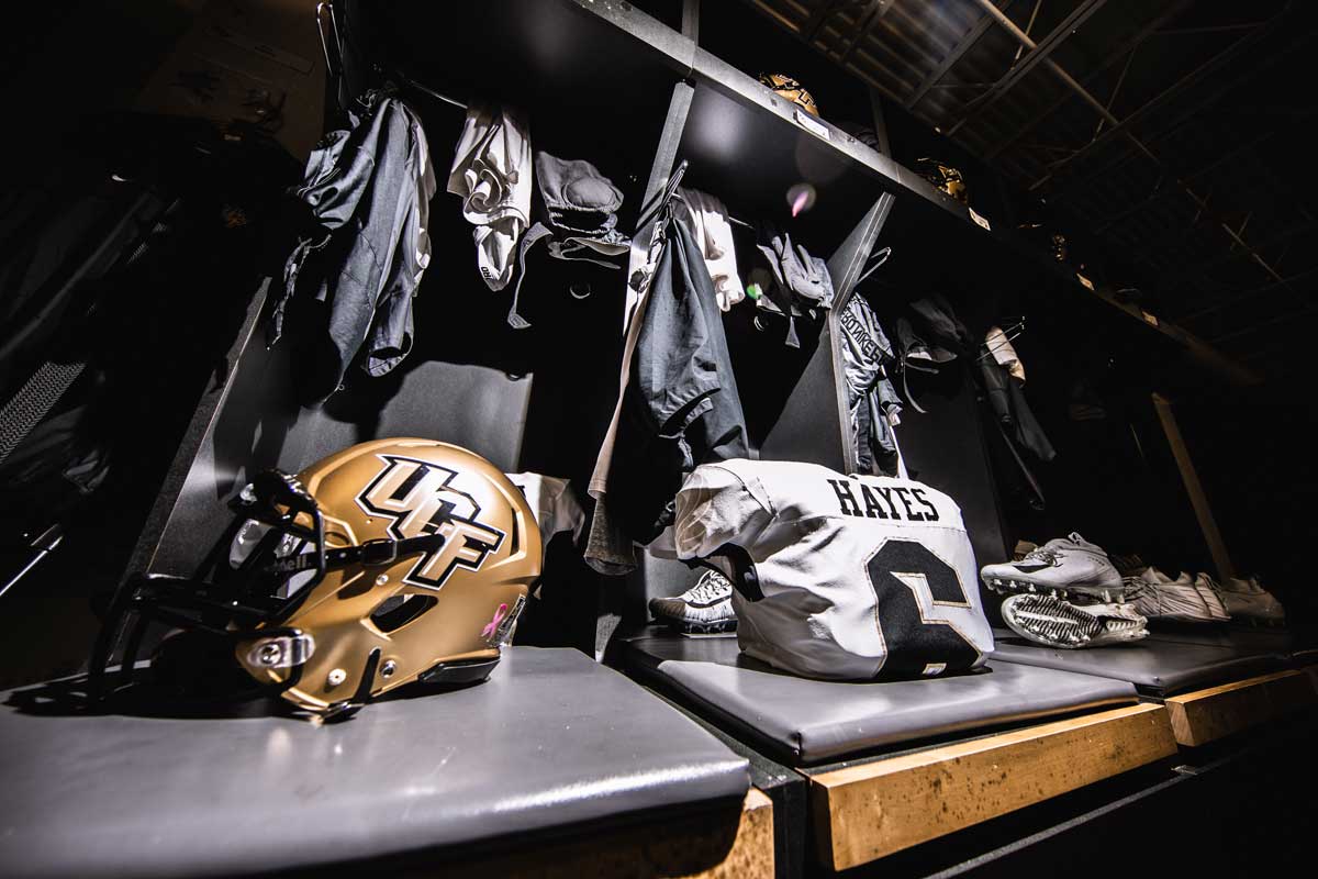 gold helmet and white #6 jersey in front of a row of lockers
