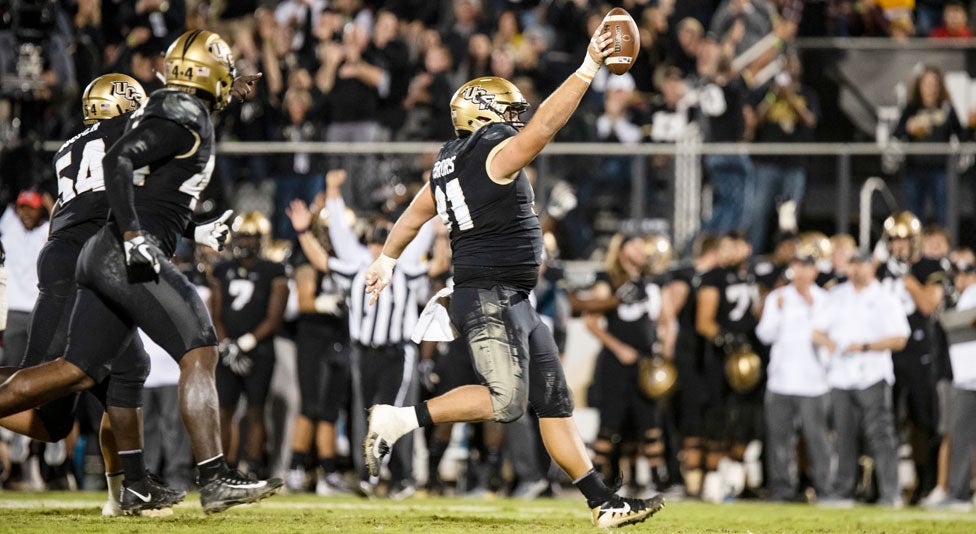 ucf defensive lineman joey connors runs into the endzone holding the football overhead with right hand