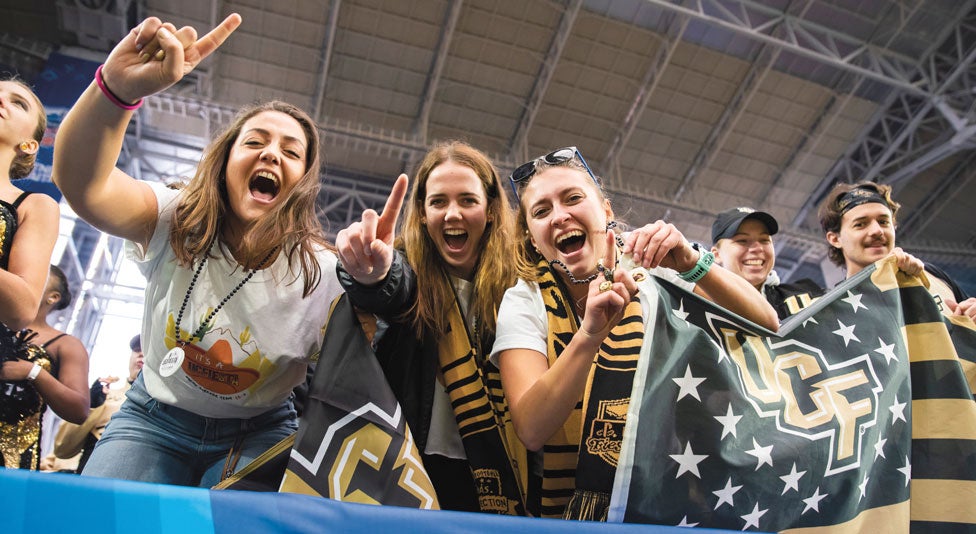 three female ucf fans holding up #1 fingers cheering on the team