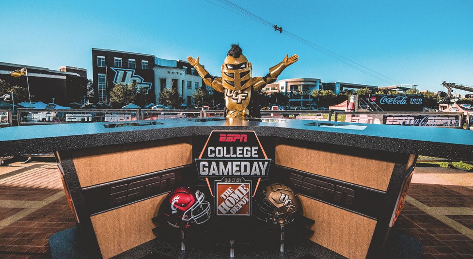 ucf mascot knightro standing with arms raised behind the espn college gameday desk