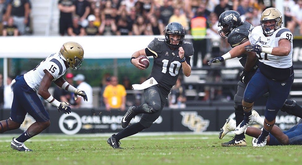 ucf quarterback mckenzie milton runs with the ball away from two navy football players