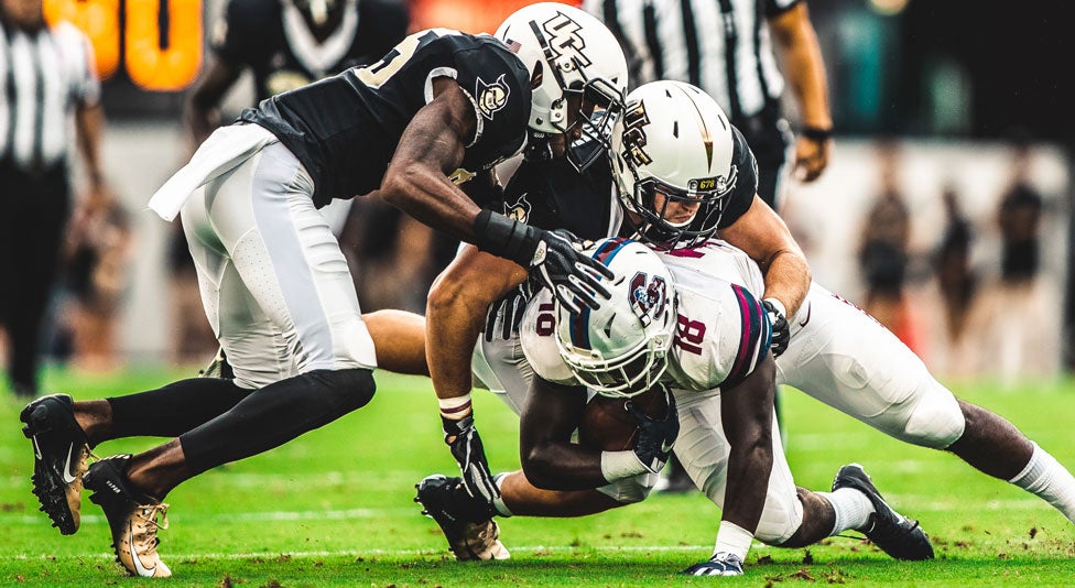 two ucf football players tackling a sc state player with the ball