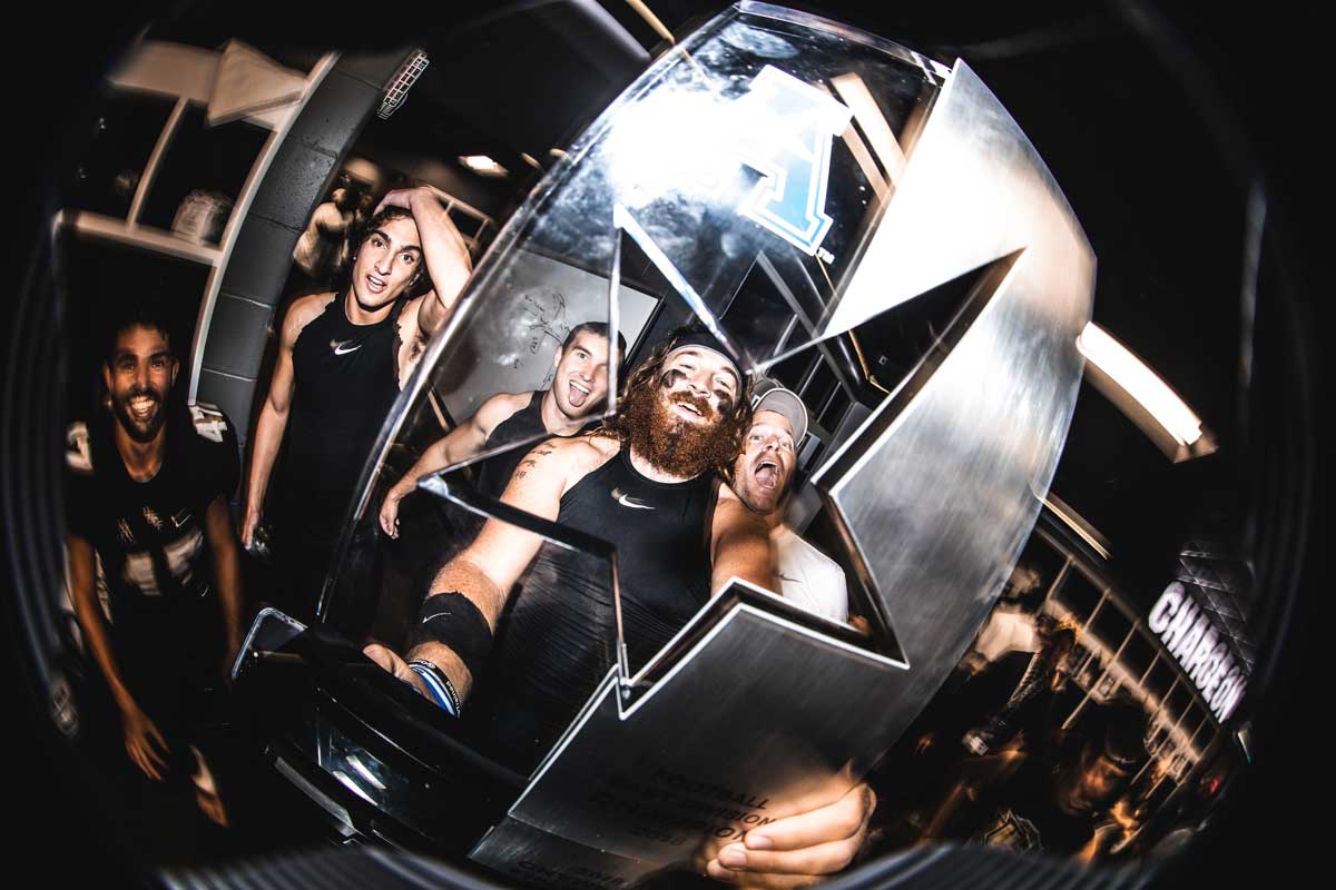 Four football players look through a star cutout on a silver trophy as they pose smiling for the camera.