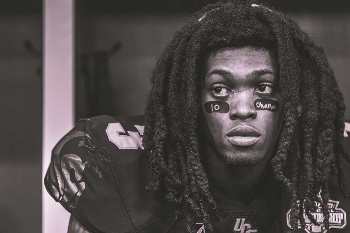 Black and white close up of UCF football player wearing #3 jersey and the message 10 and Ohana on his eye black.