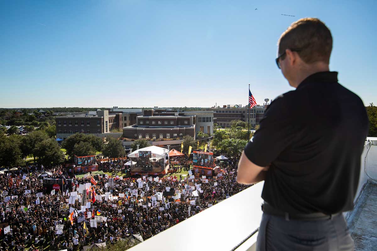 UCF director of athletics Danny White gauzes down from a rooftop at thousands gathered on Memory Mall on a sunny day