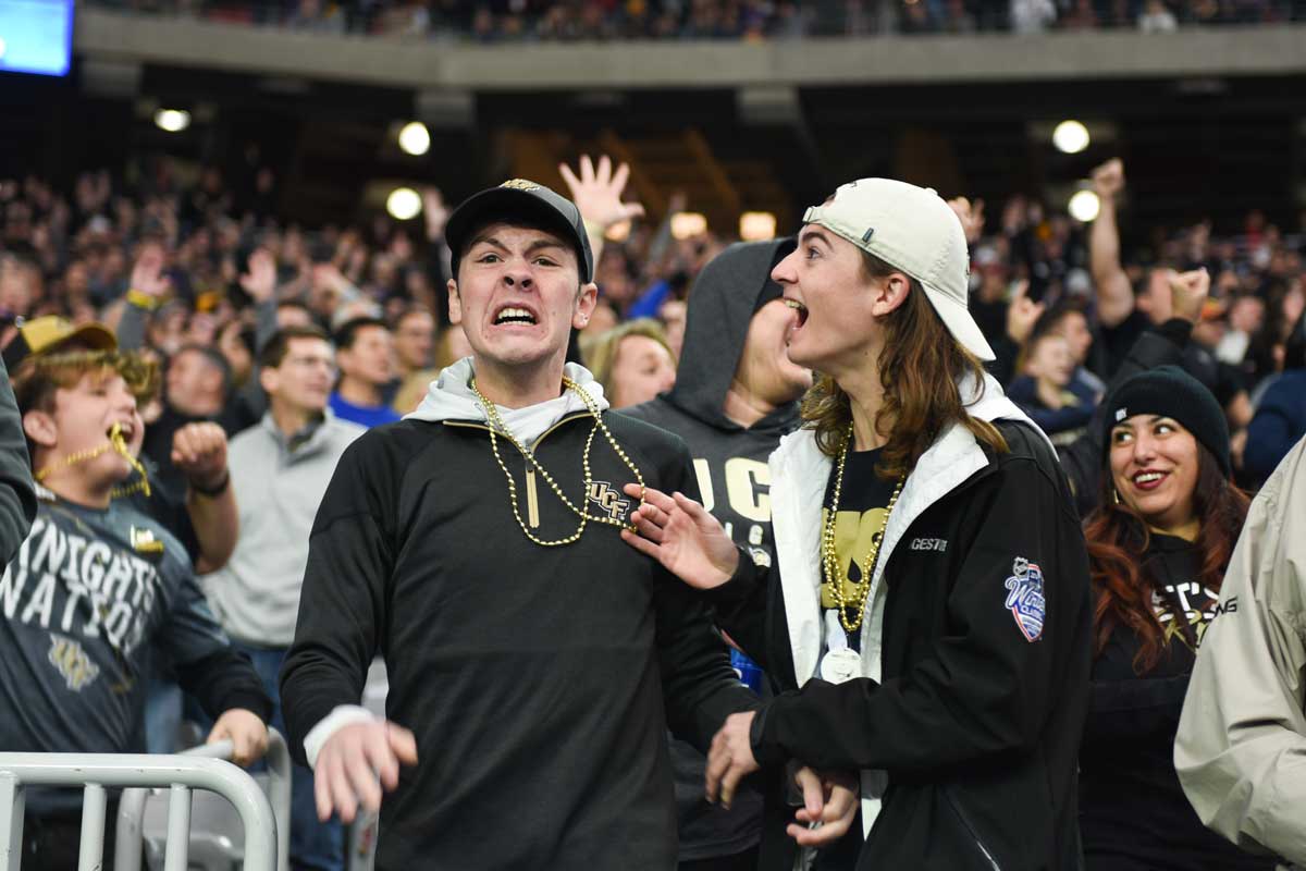 Two college-aged males wearing black long sleeve shirts stand and yell in the crowd at the ucf stadium.