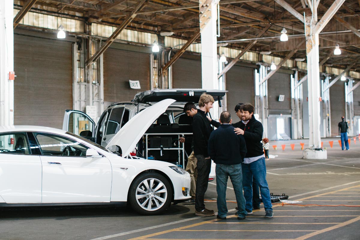 A group of men gather near two vehicles in an industrial space.