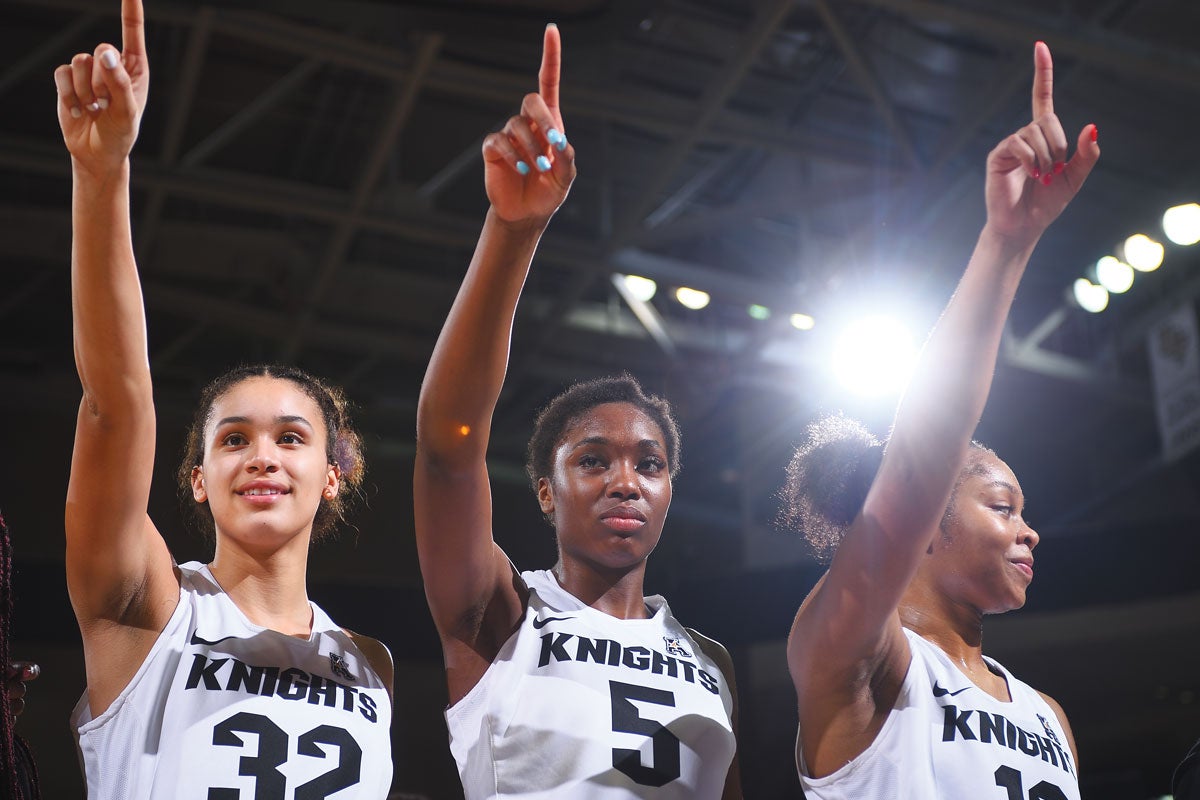 Three female basketball players hold up their pointer fingers.