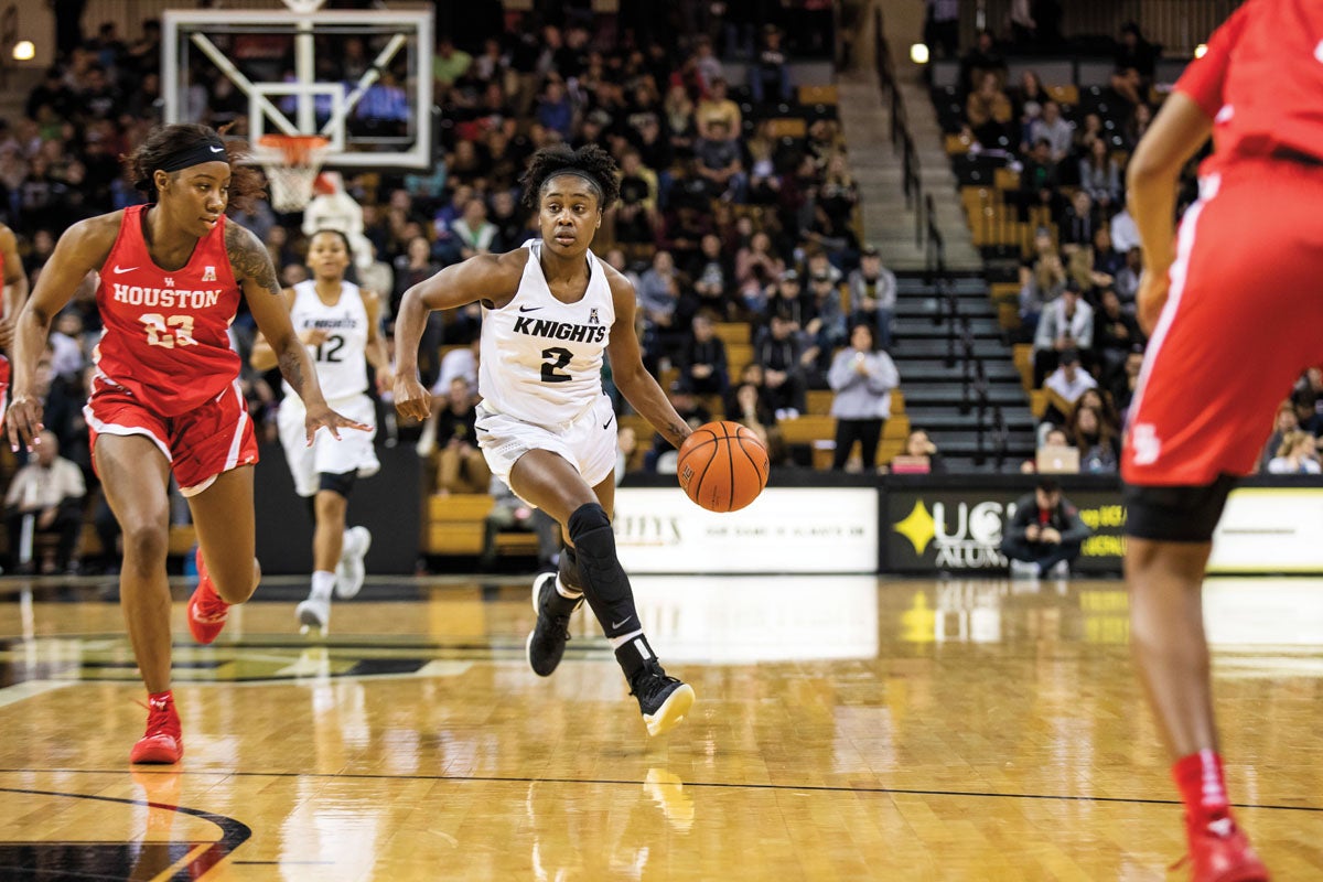 A female basketball player makes her way down the court with the ball.